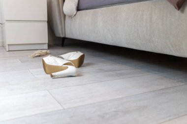 Gri bir yatağın önünde beyaz topuklu ve iç çamaşırı. Yüksek kalite fotoğraf