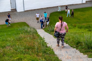 Arkadan bir kadın çim tepesindeki eski bir merdivenden aşağı iniyor, insanlar yerde toplanıyor. Yüksek kalite fotoğraf