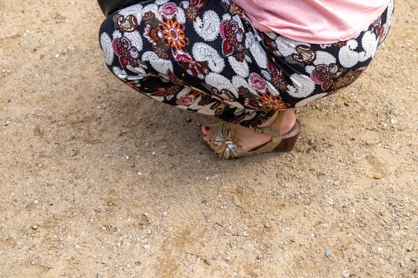 Women\'s feet in high wedge heels and airy summer pants stands on sand. High quality photo