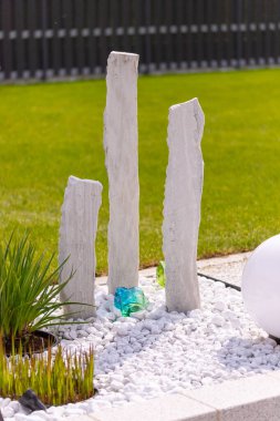Bir mermer çakıl yatağında üç mermer sütun ve arka planda birkaç bitki. Yüksek kalite fotoğraf