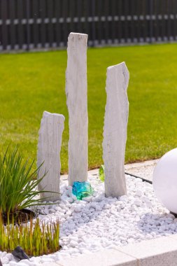 Bir mermer çakıl yatağında üç mermer sütun ve arka planda birkaç bitki. Yüksek kalite fotoğraf