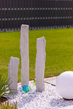 Bir mermer çakıl yatağında üç mermer sütun ve arka planda birkaç bitki. Yüksek kalite fotoğraf