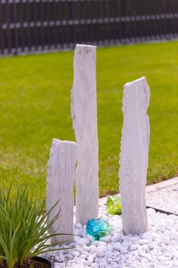 Bir mermer çakıl yatağında üç mermer sütun ve arka planda birkaç bitki. Yüksek kalite fotoğraf