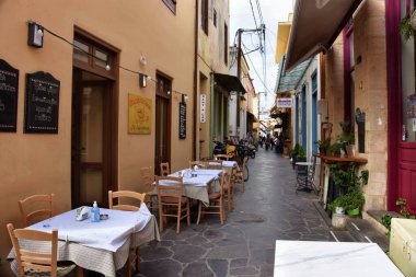 Aegina, Yunanistan - 19 Ekim 2021: Yunanistan 'ın Aegina kentindeki dar sokaktaki bir restoranın önündeki masalar.