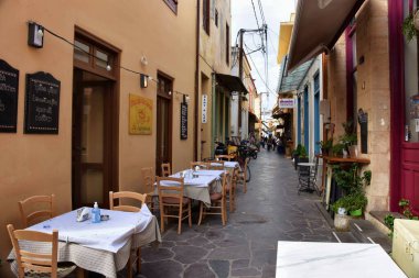 Aegina, Yunanistan - 19 Ekim 2021: Yunanistan 'ın Aegina kentindeki dar sokaktaki bir restoranın önündeki masalar.