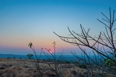 A sunset over a mountain. The sun's rays shining on the peaks create a range of colors, from warm oranges and yellows to cool purples and blues. 