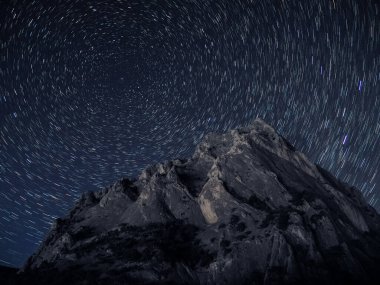 Gökyüzünde yıldız izi olan kayalık bir dağ.