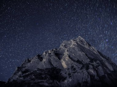 Gökyüzünde yıldız izi olan kayalık bir dağ.