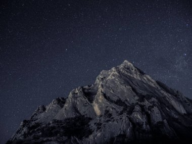 Gökyüzünde yıldız izi olan kayalık bir dağ.