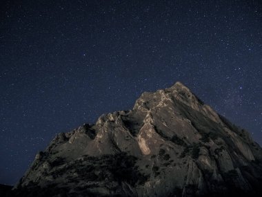 Gökyüzünde yıldız izi olan kayalık bir dağ.