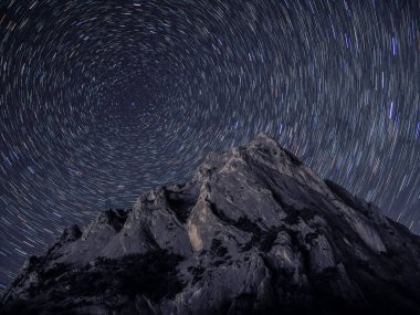 Gökyüzünde yıldız izi olan kayalık bir dağ.