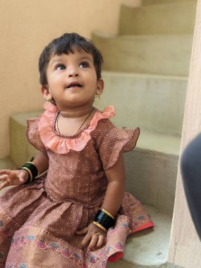 Gülümseyen kız portresi basamaklarda oturuyor, sevimli bir ifadeyle geleneksel yeşil bilezikler takıyor. 