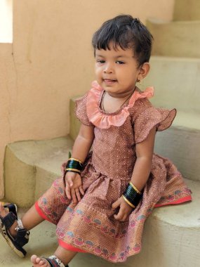 Gülümseyen kız portresi basamaklarda oturuyor, sevimli bir ifadeyle geleneksel yeşil bilezikler takıyor. 