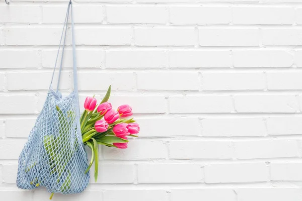 Bouquet of pink tulips in a mesh bag against a white brick wall. High quality photo