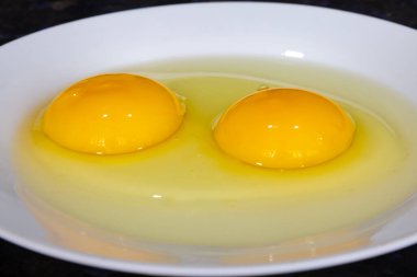 Koyu arka planda beyaz tabakta iki yumurta sarısı ve seçici odaklanma. Yakın çekim.