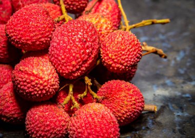 Olgun liçi meyvesi (Litchi chinensis) koyu arka planda izole edilmiş ve seçici bir odak noktasıdır. Kırmızı meyveler