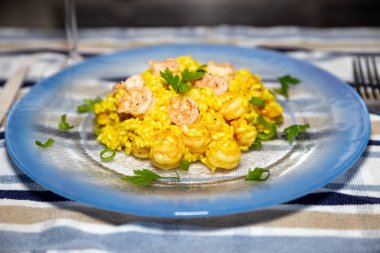 Classic shrimp risotto with arborio rice and saffron, garnished with fresh parsley and chives. Blue plate