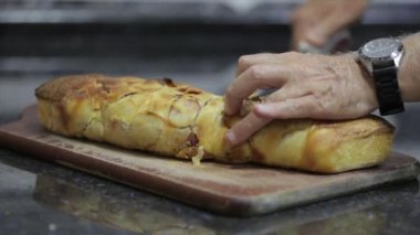 Pepperoni bread coming out of the warm oven and being sliced with a serrated knife.