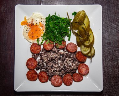 Geleneksel Brezilya yemeği, fasulye, sosis, yumurta, lahana ve mayalanmış salatalık.