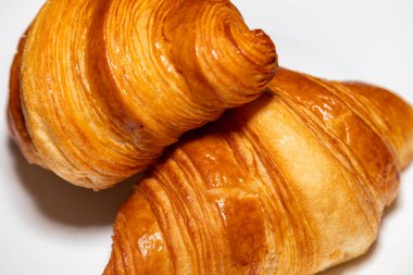 Sade arka planda gölgesi olan altın rengi tereyağlı kruvasan..