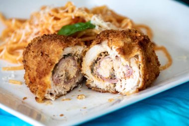 Geleneksel tavuk Kiev, ekmekli, doldurulmuş ve kızartılmış domates soslu spagetti ve rendelenmiş parmesan peyniri ile servis ediliyor.