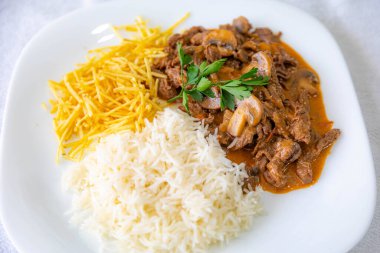 Geleneksel fileminyon mantarlı stroganoff, patates kızartması ve pilav.