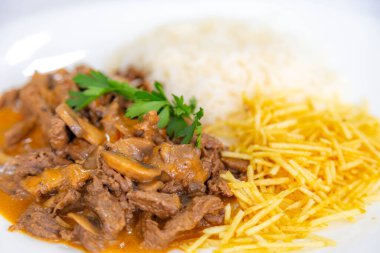 Geleneksel fileminyon mantarlı stroganoff, patates kızartması ve pilav.