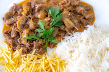 Geleneksel fileminyon mantarlı stroganoff, patates kızartması ve pilav.