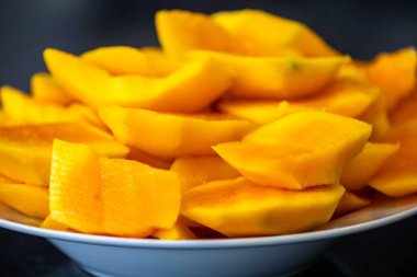 Koyu arkaplanda izole edilmiş tabakta olgun mango dilimleri.