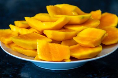 Koyu arkaplanda izole edilmiş tabakta olgun mango dilimleri.