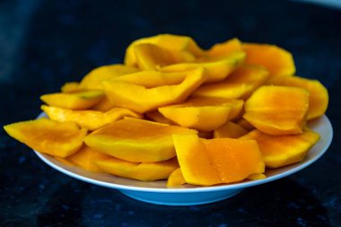 Koyu arkaplanda izole edilmiş tabakta olgun mango dilimleri.
