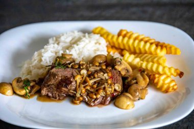 Lüks ve enfes bir yemek, mantar soslu fileminyon yanında da beyaz pirinç ve patates kızartması. Pas soslu fileminyon.