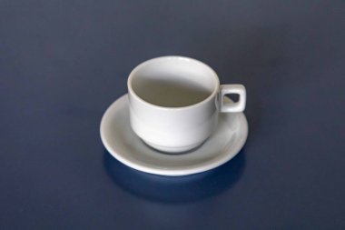 Mavi bir yüzey üzerinde beyaz seramik fincan ve çay tabağı.