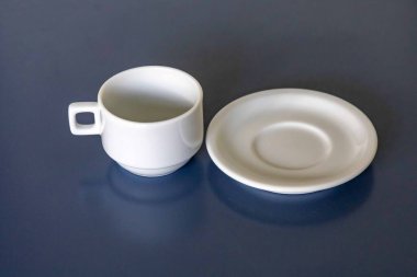 Mavi bir yüzey üzerinde beyaz seramik fincan ve çay tabağı.