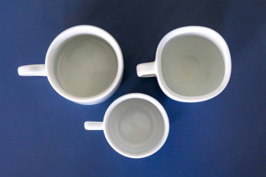 Mavi bir yüzey üzerinde beyaz seramik fincan ve çay tabağı.