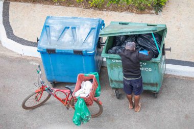 Brezilya, 8 Ağustos 2025, şortlu, şapkalı ve parmak arası terlikli, tanımlanamayan, yukarıdan görülen geri dönüşüm için çöp toplayan adam