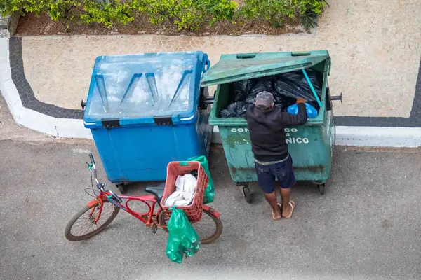 Brezilya, 8 Ağustos 2025, şortlu, şapkalı ve parmak arası terlikli, tanımlanamayan, yukarıdan görülen geri dönüşüm için çöp toplayan adam