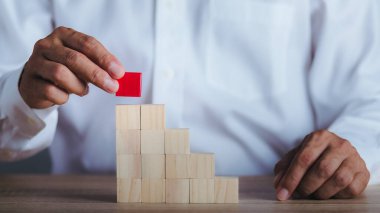 A young businessman is putting down the last piece of red wood block