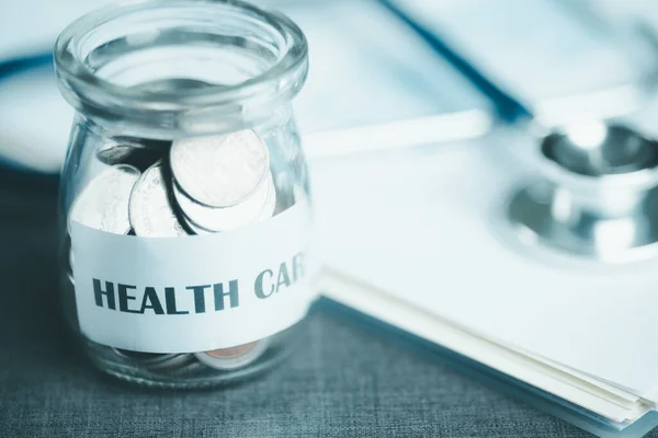 message on paper and coins in glass jar, stethoscope and medical report, all on table, savings concept, for health care expenses, financial health check, control financial risks, insurance investments