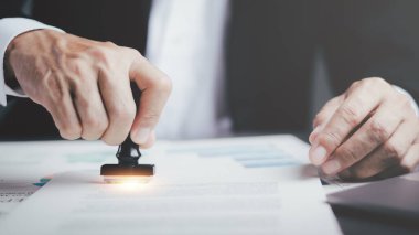 A young executive is stamping on documents for a business contract. Transaction and document management concepts include negotiating corporate entities and filling out legal forms or agreements.