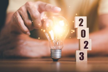 New Year 2023 Beginning Concept,,concept with innovation and inspiration, innovative technology in science concept and modern business development,creative idea,Wooden blocks and light bulbs on table
