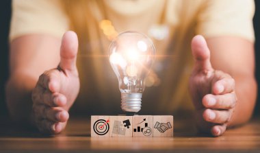 Light bulbs placed on wooden blocks and human hands on table ,target ideas and business strategies,through planning and teamwork To analyze and develop company performance from growth data to future