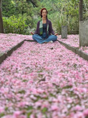 Kiraz çiçekleriyle kaplı bir yolda huzur içinde meditasyon yapan bir kadın. Arka plandaki bereketli doğa ve sükunetin atmosferi iç huzuru ve ruhsal bağlantıyı artırıyor..