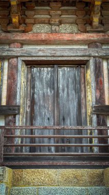 Etkileyici ahşap bir kapı, zengin dokusu ve kırsal detayları olan, eski bir yapıda. Tarihsel kökler ve zamanın patinası geçmişe özlem ve takdiri çağrıştırıyor. Tahta kahverengi ve gri tonlarını gösteriyor, aşınma izleri var..