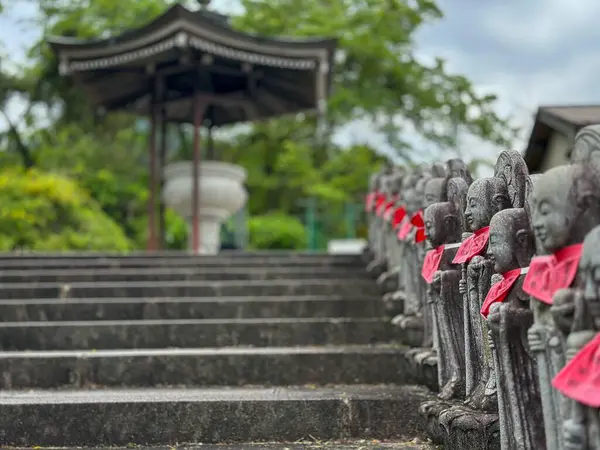 Kırmızı kurdelelerle süslenmiş, merdiven boyunca uzanan heykel manzarası. Arka planda, bulutlu bir gökyüzünün altındaki bir pavyon sahneyi huzur ve ruhani bir yansımaya dönüştürür..