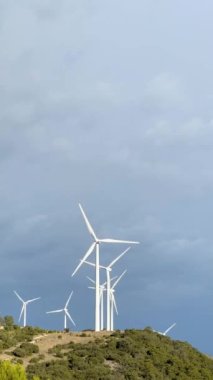 Vertical video of a group of windmills generating power on top of a hill with a dramatic electric blue sky in the background. High-quality FullHD footage. High-quality FullHD footage