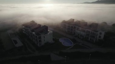 Top view drone footage of afternoon winter fog moving across houses on top of the hill in Spain. High-quality FullHD footage