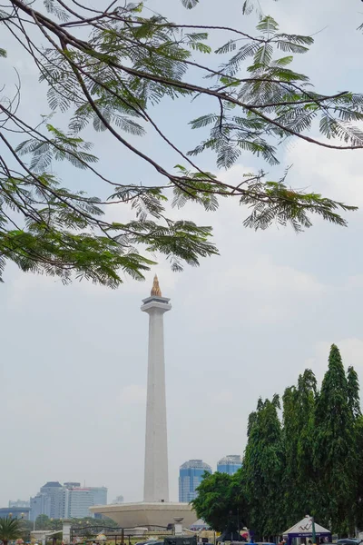 Vertical lateral image of Jakarta National Monument on a sunny day behind some tree branches. High-quality photo