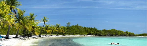 Huge panoramic image of a family enjoying the clear waters of an amazing beach in paradise. High-quality panoramic photography