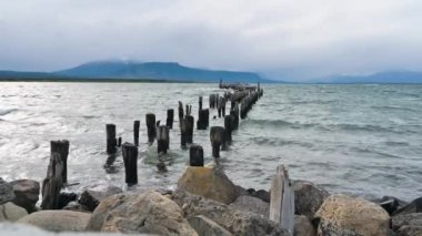Old Puerto Natales pier with wind-blowing waves and mountains, Puerto Natales, Chilean Patagonia, Chile - stock video.